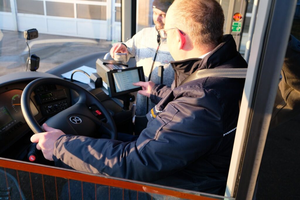 Busfahrer am Steuer eines Bottenschein-Reisebusses, der den Bildschirm eines Tablets betrachtet.