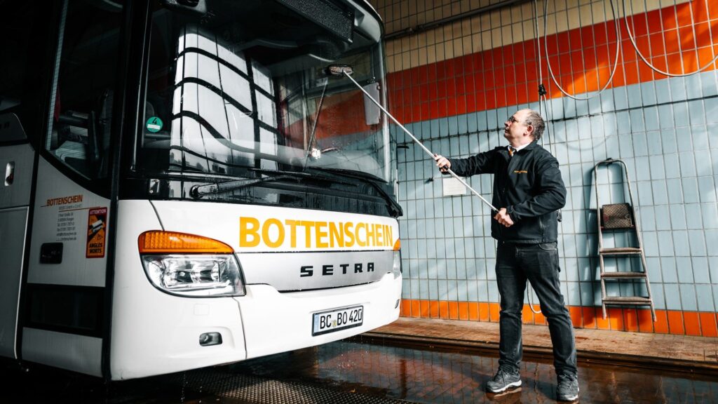 Ein Mitarbeiter von Bottenschein Reisen reinigt einen Bus in einer Halle.