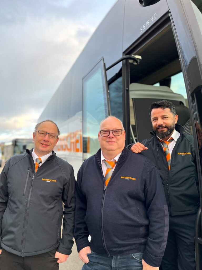 Drei Mitglieder des Bottenschein-Reisen-Teams laecheln vor einem Reisebus.