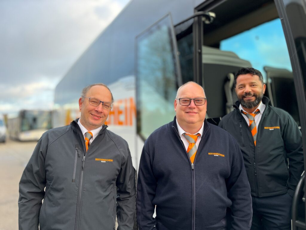 Drei Teammitglieder von Bottenschein Reisen stehen mit einem Reisebus im Hintergrund.