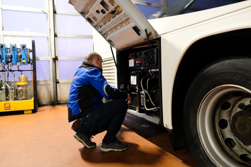 Ein Mechaniker ueberprueft den Motor eines Busses in einer Werkstatt.